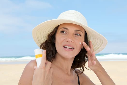 Beautiful woman at the beach putting sunscreen on her body