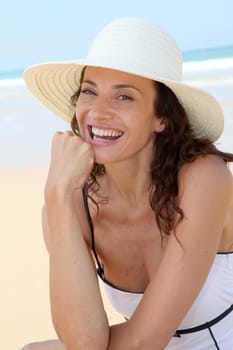 Beautiful woman sitting on the beach with straw hat