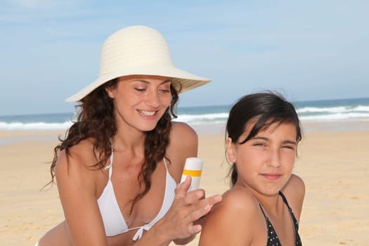 Mother spreading sunscreen on her daughter's shoulders