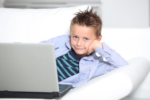 Blond little boy sitting on sofa with laptop computer