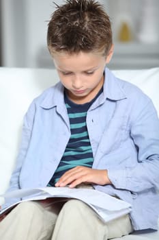 Blong little boy sitting on sofa with book