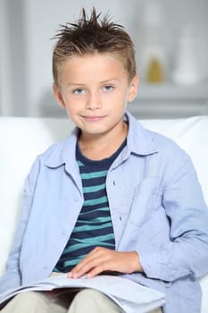 Blong little boy sitting on sofa with book