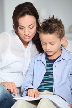 Littme boy and mother sitting on sofa at home with book