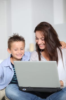 Little boy and mother sitting on sofa at home with laptop