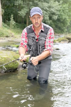 Fisherman in river with fishing rod