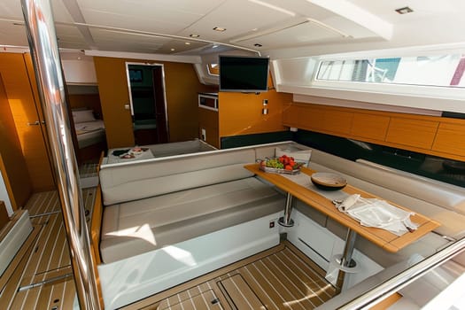 Luxurious modern yacht interior with dining area and tv in sunlit cabin.