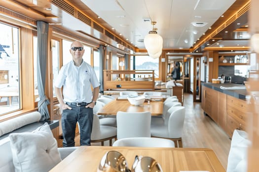 An adult man in sunglasses standing inside a luxurious inner yacht with wooden decor.