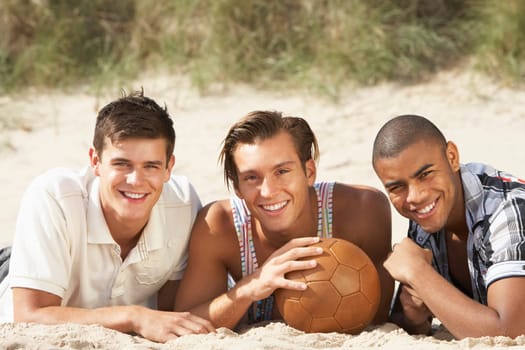 Three Young Men Relaxing On Beach With Football Together