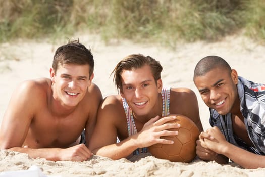 Three Young Men Relaxing On Beach With Football Together