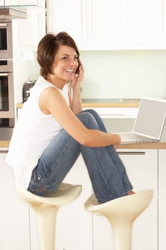 Young Woman Relaxing Sitting In Kitchen Talking On Phone