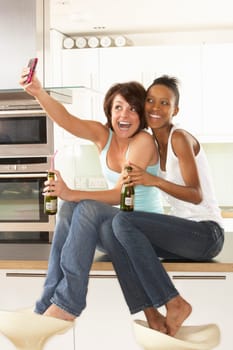 Two Girlfriends Taking Photo With Digital Camera In Modern Kitchen