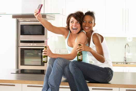 Two Girlfriends Taking Photo With Digital Camera In Modern Kitchen