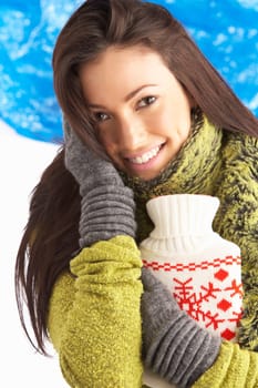 Young Woman Wearing Warm Winter Clothes Holding Hot Water Bottle In Studio