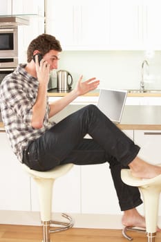 Young Man Relaxing Sitting In Kitchen Talking On Phone
