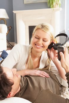 Couple Listening To MP3 Player On Headphones Relaxing Laying On Rug At Home