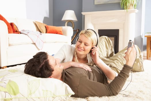 Couple Listening To MP3 Player On Headphones Relaxing Laying On Rug At Home