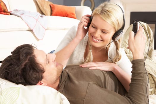 Couple Listening To MP3 Player On Headphones Relaxing Laying On Rug At Home