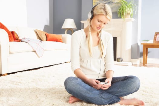 Woman Listening To MP3 Player On Headphones Relaxing Sitting On Rug At Home