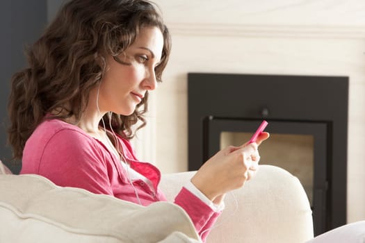 Woman Listening To MP3 Player On Headphones Relaxing Sitting On Rug At Home