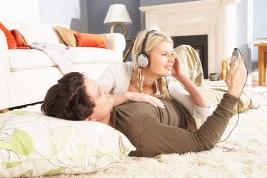 Couple Listening To MP3 Player On Headphones Relaxing Laying On Rug At Home