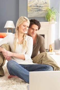 Couple Using Laptop Relaxing Sitting On Rug At Home