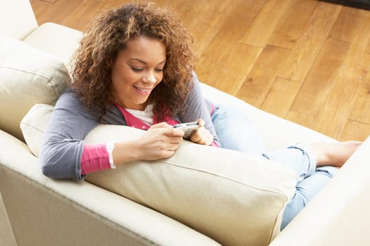 Woman Looking At Pictures On Digital Camera Relaxing Sitting On Sofa At Home