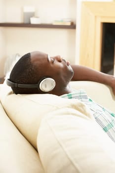 Young Man Relaxing Sitting On Sofa Listening to Music At Home On Headphones