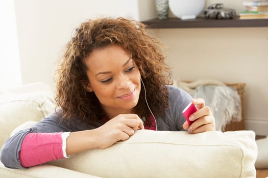 Woman Listening To MP3 Player On Headphones Relaxing Sitting On Rug At Home