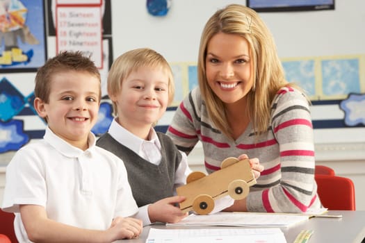 Two Male Primary School Pupils And Teacher Working At Desk In Classroom