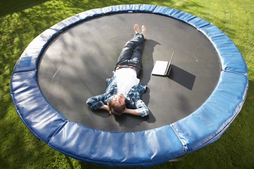 Young Man Relaxing On Trampoline With Laptop