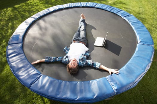 Young Man Relaxing On Trampoline With Laptop