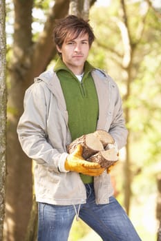 Man Outdoors In Autumn Woodland Gathering Logs