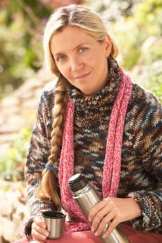 Young Woman Relaxing With Thermos Flask In Autumn Landscape
