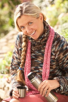 Young Woman Relaxing With Thermos Flask In Autumn Landscape