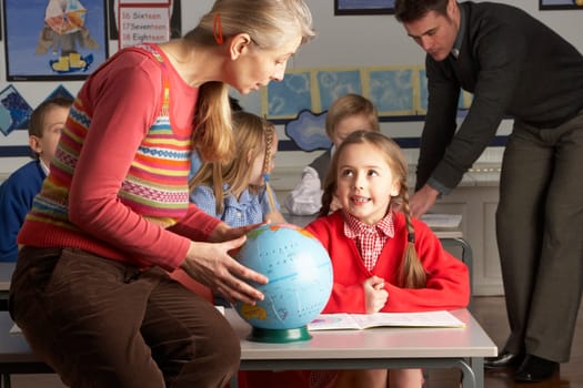 Teachers Giving Geography Lesson To Primary School Children In Classroom