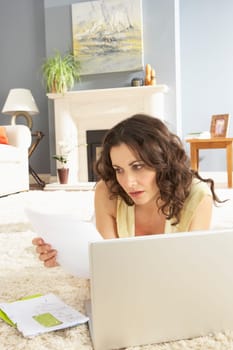 Woan Using Laptop To Manage Household Bills Laying On Rug At Home