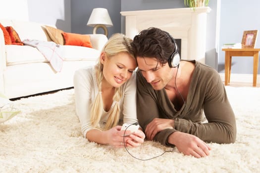 Couple Listening To MP3 Player On Headphones Relaxing Laying On Rug At Home