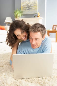 Couple Using Laptop Relaxing Laying On Rug At Home
