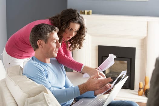 Couple Using Laptop And Discussing Household Bills Sitting On Sofa At Home