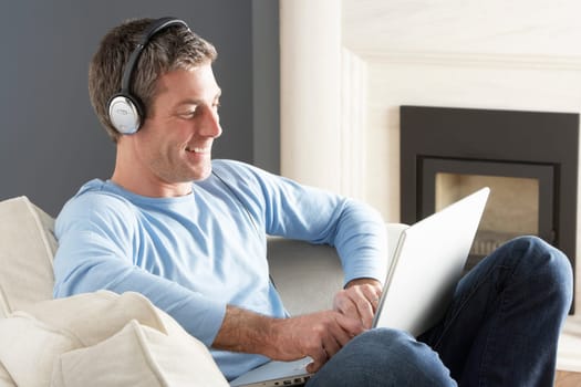 Man Using Laptop Wearing Headphones Relaxing Sitting On Sofa At Home