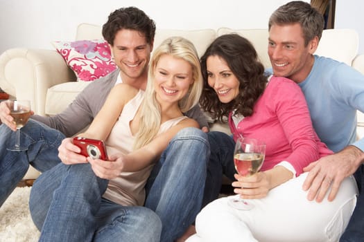 Group Of Friends Looking At Pictures On Digital Camera At Home