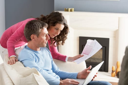 Couple Using Laptop And Discussing Household Bills Sitting On Sofa At Home