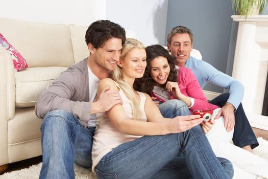 Group Of Friends Looking At Pictures On Digital Camera At Home