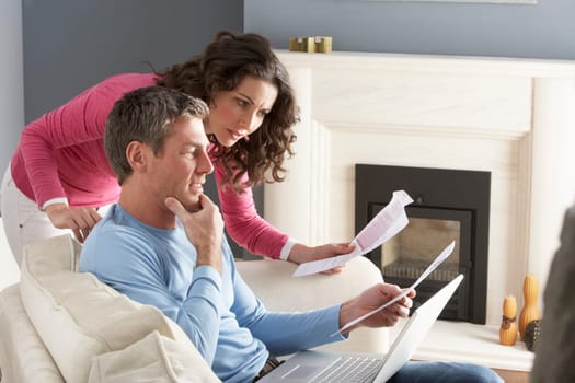 Couple Using Laptop And Discussing Household Bills Sitting On Sofa At Home