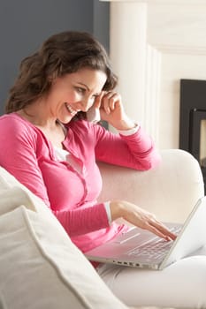 Woman Using Laptop Relaxing Sitting On Sofa At Home Talking On Phone