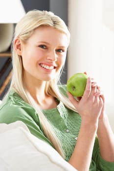 Woman Relaxing On Sofa Eating Apple At Home
