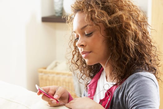 Woman Listening To MP3 Player On Headphones Relaxing Sitting On Rug At Home