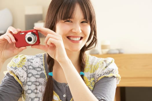 Young Woman Taking Photograph On Digital Camera At Home