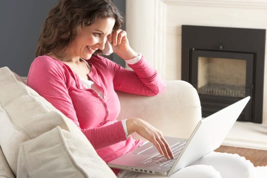 Woman Using Laptop Relaxing Sitting On Sofa At Home Talking On Phone