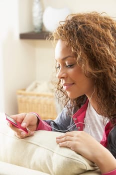 Woman Listening To MP3 Player On Headphones Relaxing Sitting On Rug At Home